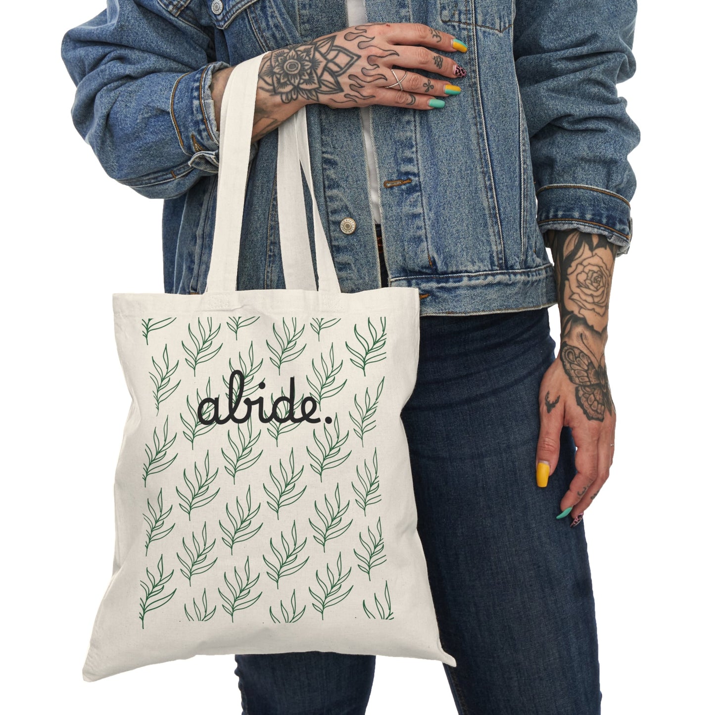 Person holding a tote bag with leaf pattern and 'alide' text, wearing a denim jacket.