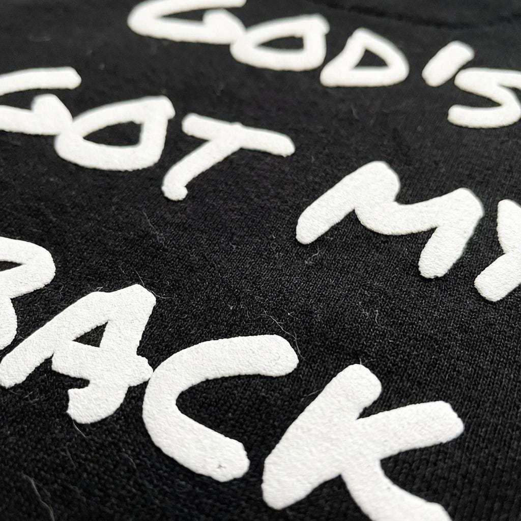 Close-up detail of black fabric featuring the phrase; in white 3D puff print lettering